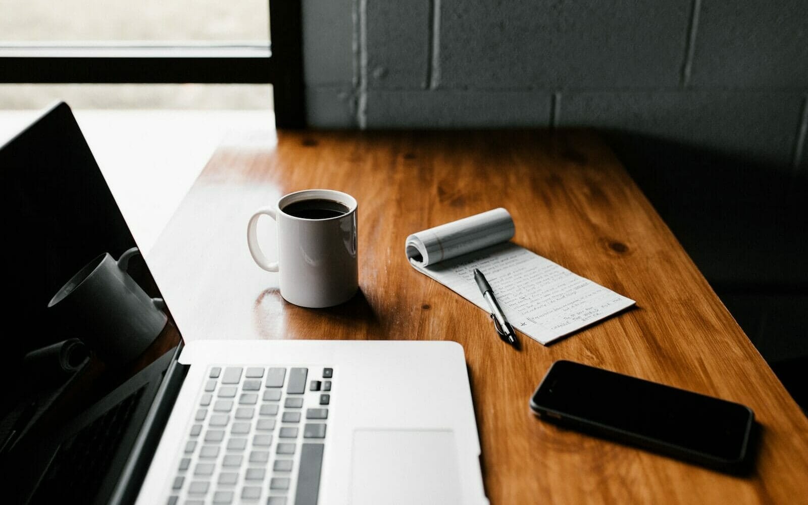 MacBook Pro, white ceramic mug,and black smartphone on table