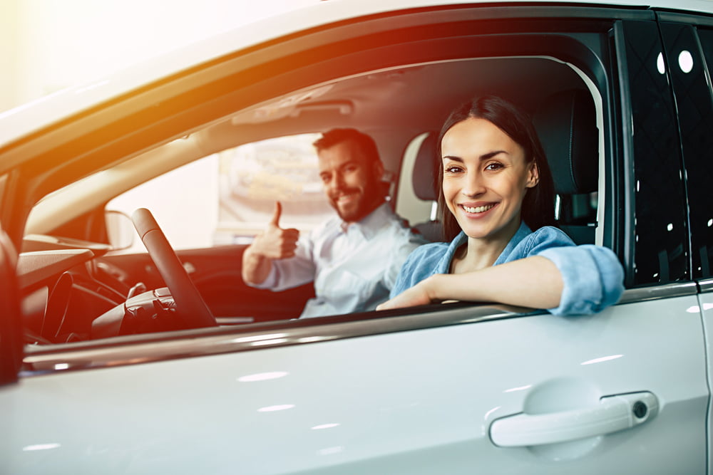 Happy couple sitting in new car in dealership choosing car concept — Photo