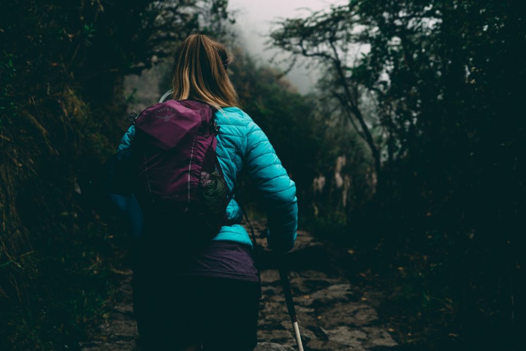 woman wearing bubble jacket walking on pathway between forest