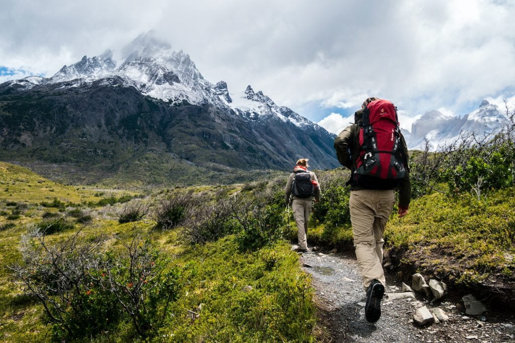 two people walking towards a mountain covered with snow while visiting South America