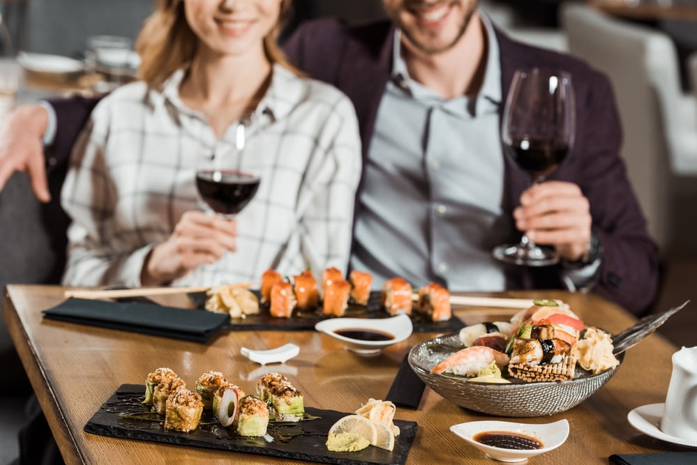 Partial view of smiling couple eating sushi and drinking wine in restaurant 