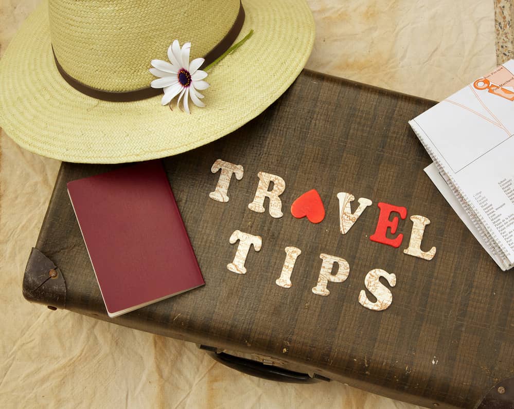Summer travel hat, flower, old suitcase, brown passport, map, and wooden letters: "travel tips"