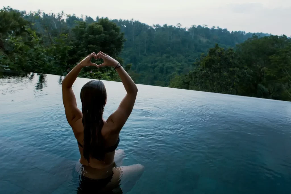 A woman making a heart with her hands in an infinity pool.