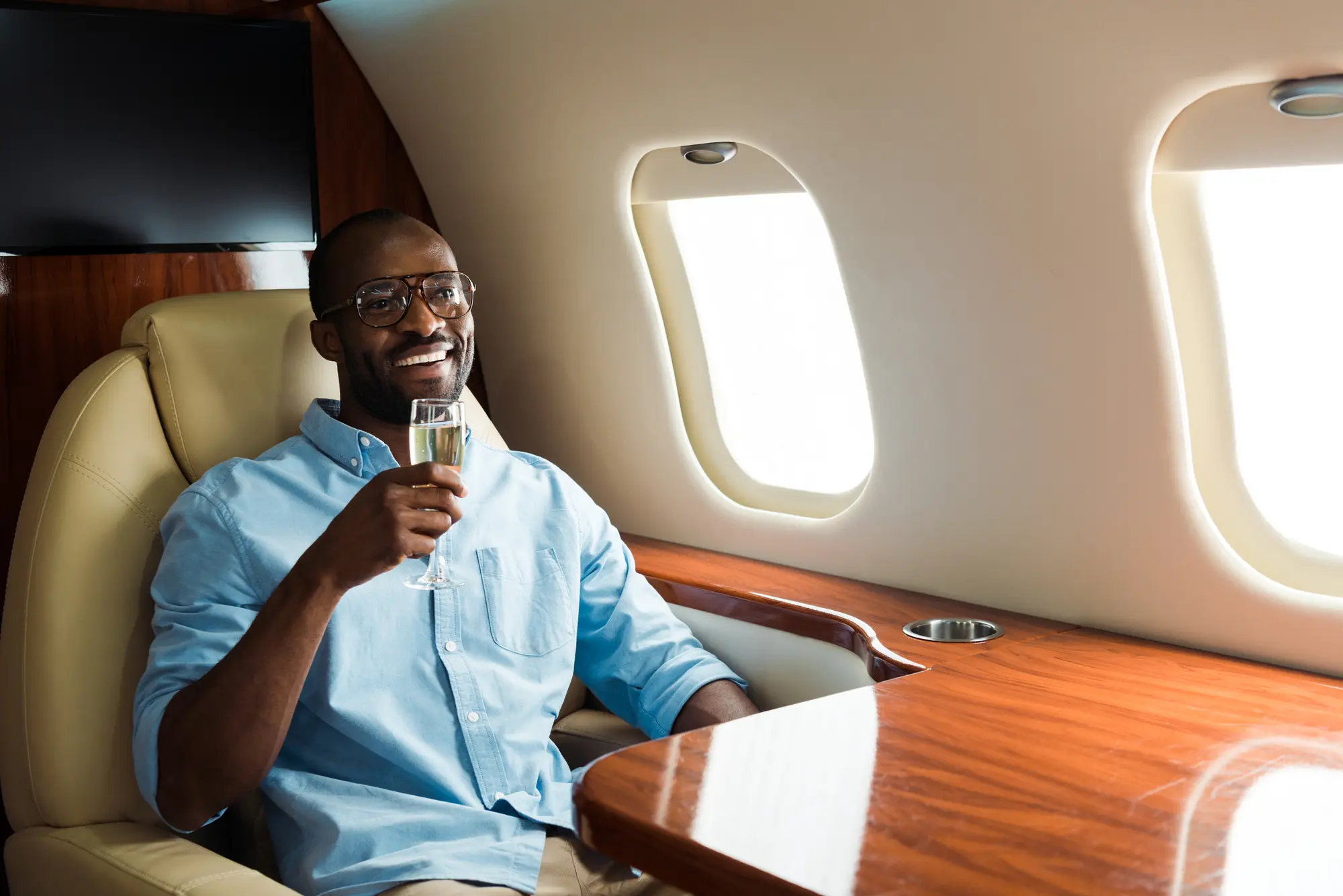 A man sitting in a plane, holding a glass of wine, and flying first class.