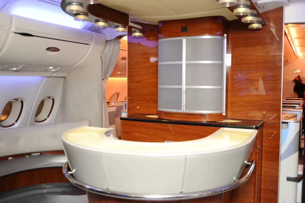 Interior of a luxury private jet featuring polished wood paneling, cream-colored leather seats, and ambient lighting.
