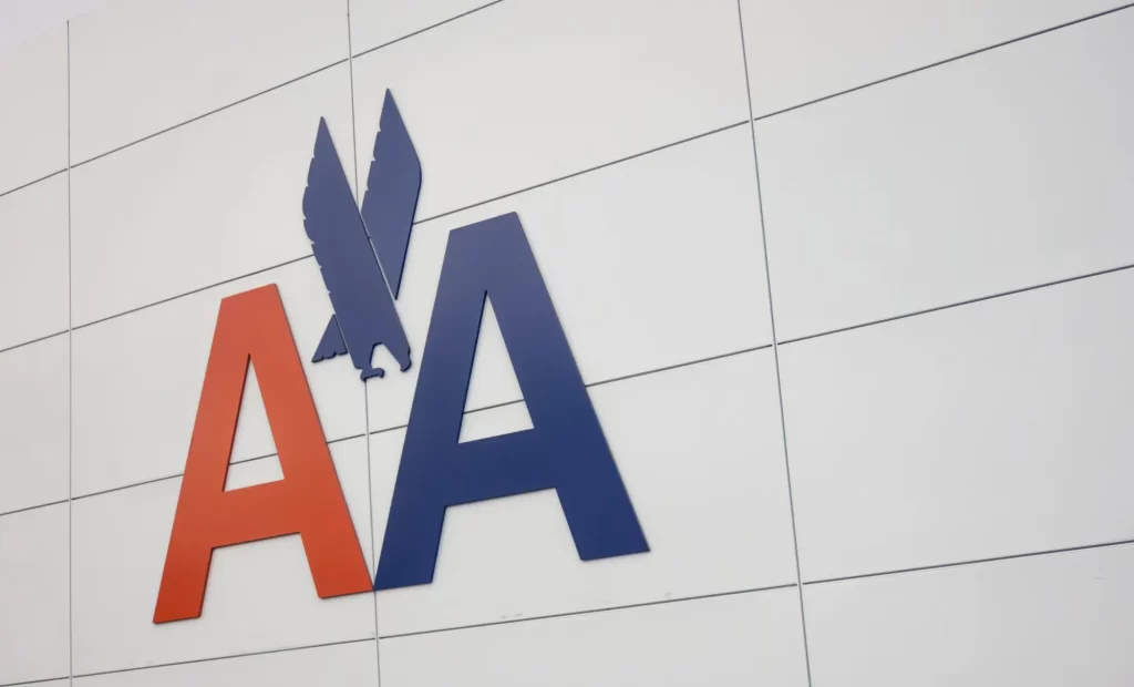 The logo of american airlines, featuring red and blue letters "aa" with a stylized eagle between the letters, mounted on a light grey tiled wall.